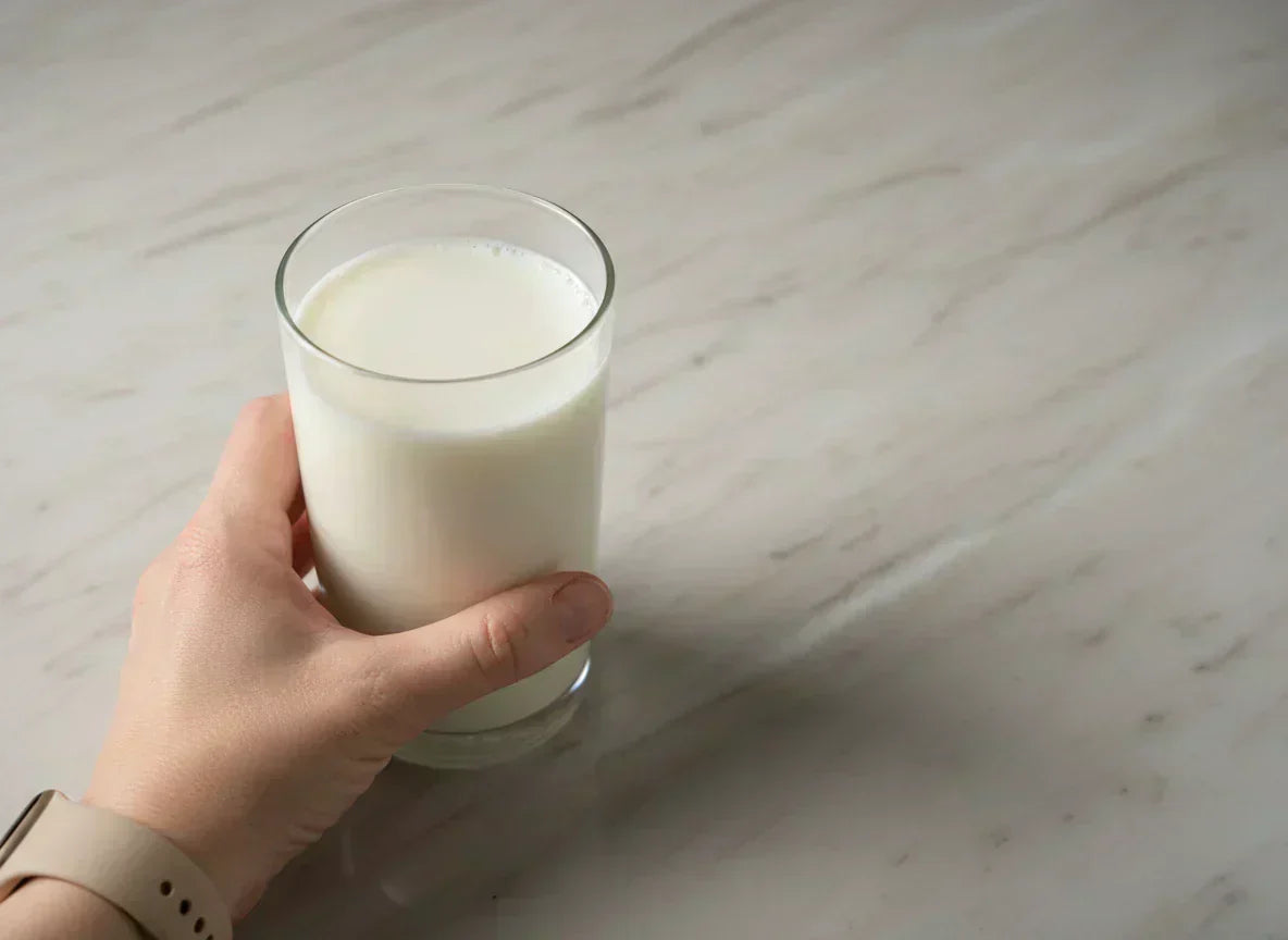 Hand holding a glass of plant-based milk on marble countertop — almond milk vs soy milk protein and nutrition comparison