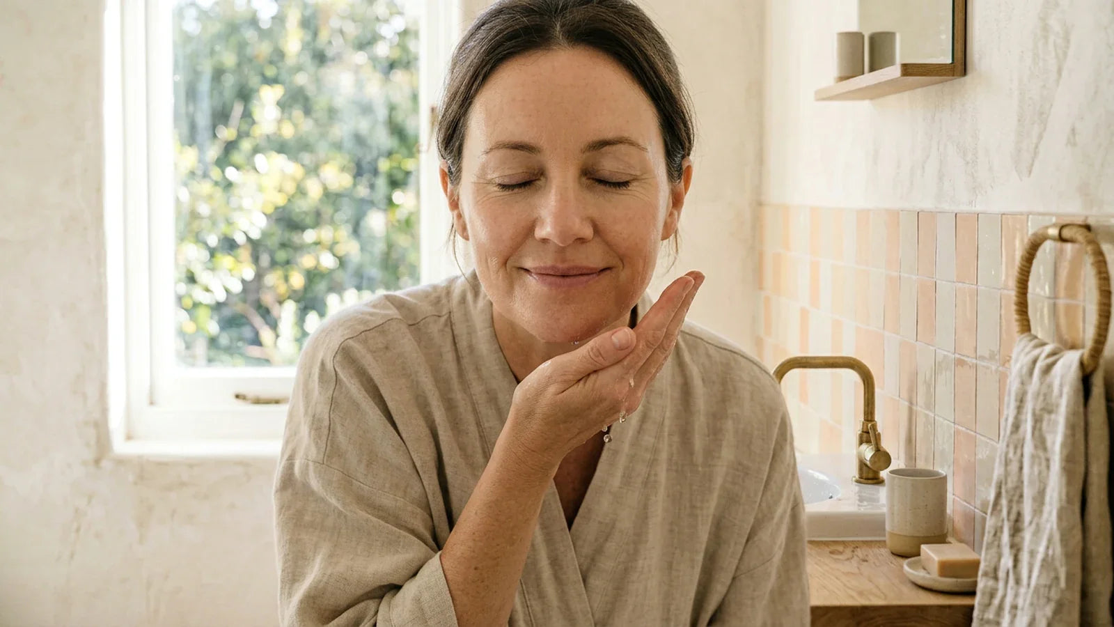Femme d'une quarantaine d'années à la peau naturellement saine, baignée par la douce lumière du matin.