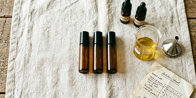 Espace de travail avec flacons roll-on ambrés vides, petit entonnoir en acier, bécher en verre et flacons d'huile ambrée sur lin
