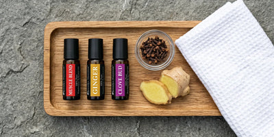 Plateau en bois avec flacons roll-on d'huile de muscade ambrée, racine de gingembre frais, clous de girofle et serviette en coton pliée sur une pierre