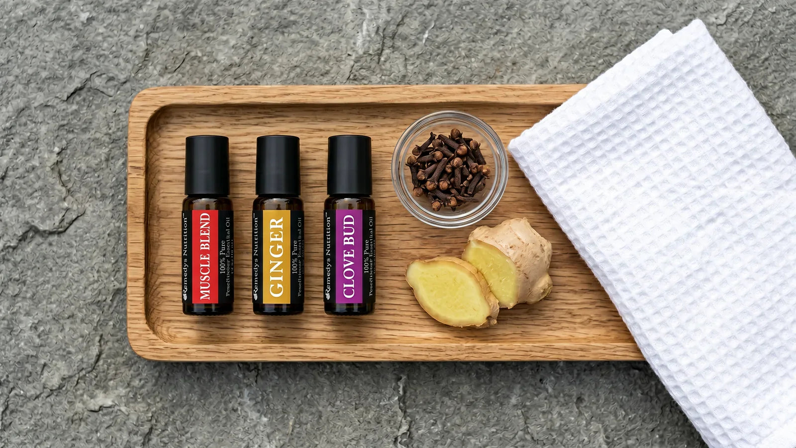 Plateau en bois avec flacons roll-on d'huile de muscade ambrée, racine de gingembre frais, clous de girofle et serviette en coton pliée sur une pierre