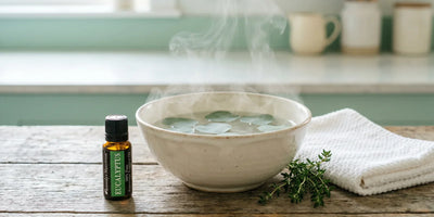 Bol d'eau chaude fumante avec des feuilles d'eucalyptus flottantes et flacon d'huile essentielle d'ambre sur un comptoir en bois
