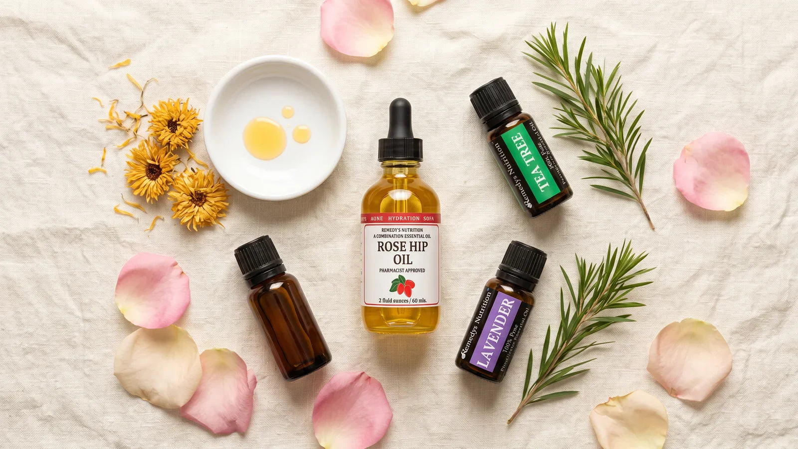 Composition à plat de produits de soin&nbsp;: flacons d’huiles essentielles ambrées, huile végétale de rose musquée, pétales de rose frais sur lin crème