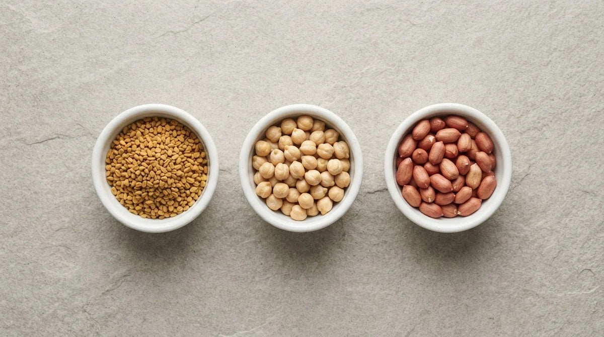 Three white dishes holding fenugreek seeds, chickpeas and peanuts on grey stone