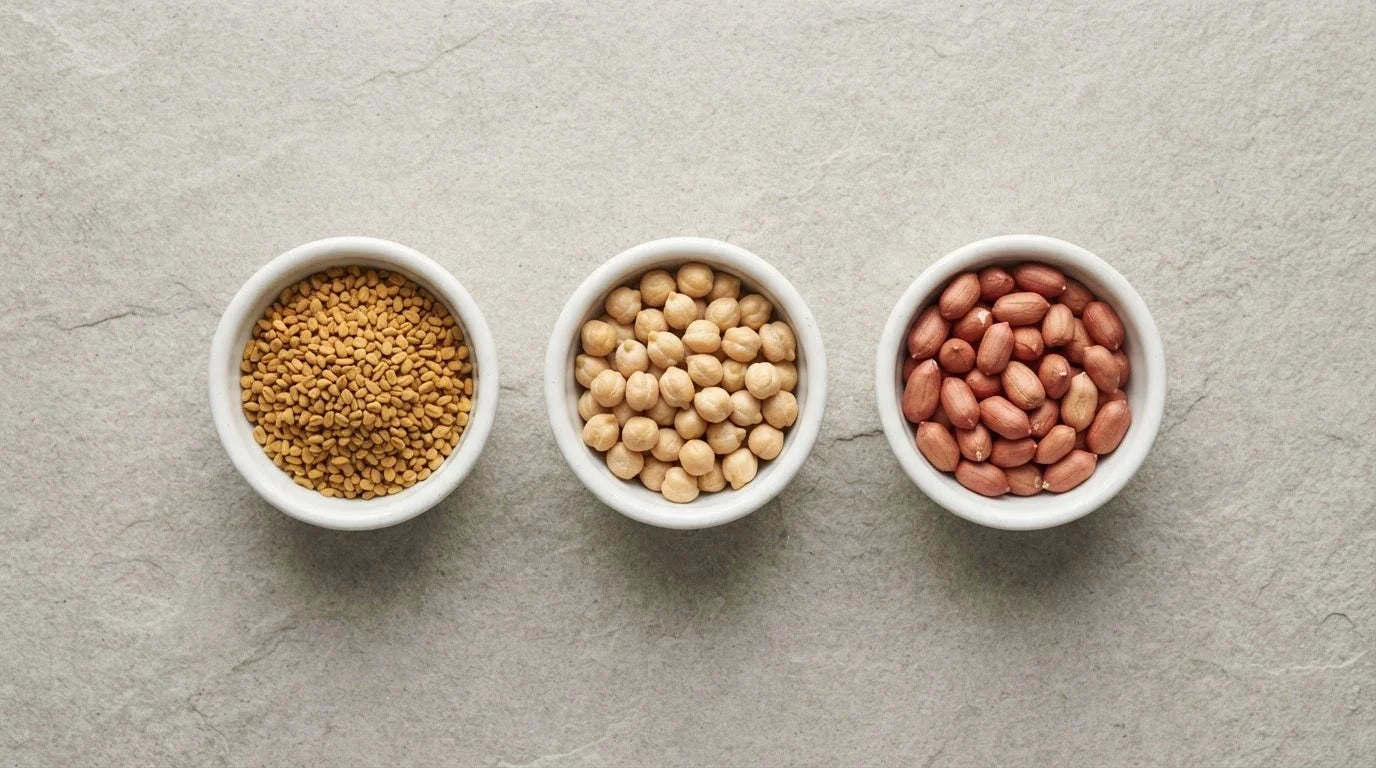 Three white dishes holding fenugreek seeds, chickpeas and peanuts on grey stone
