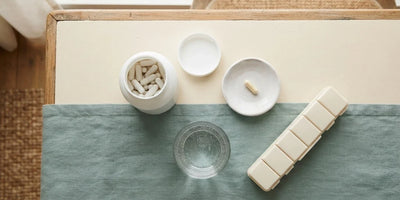 Overhead view of a white jar, one cream capsule on a dish, a glass of water and a plain pill organiser