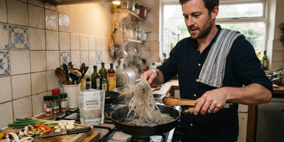 A man dry-frying translucent shirataki noodles in a hot pan