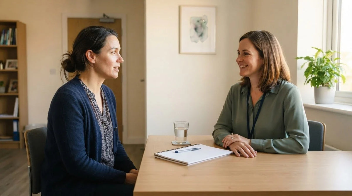 A woman talking with a clinician across a plain desk in a consulting room