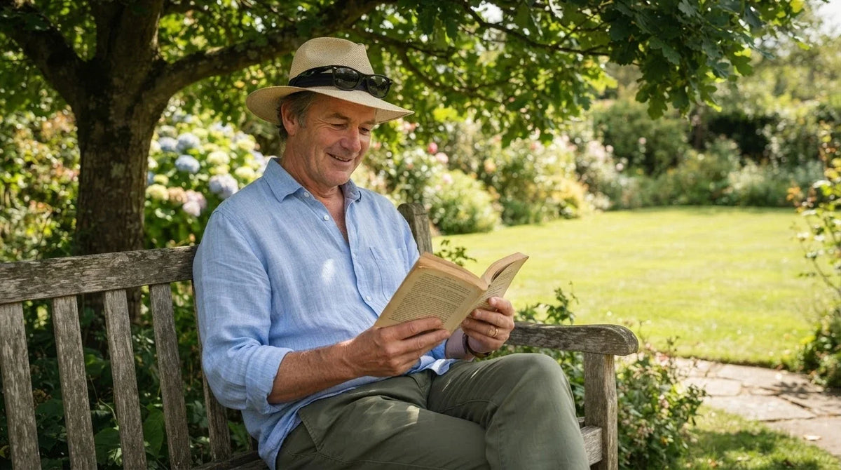 A man in a straw hat and long sleeves reading in the shade of a tree on a sunny day