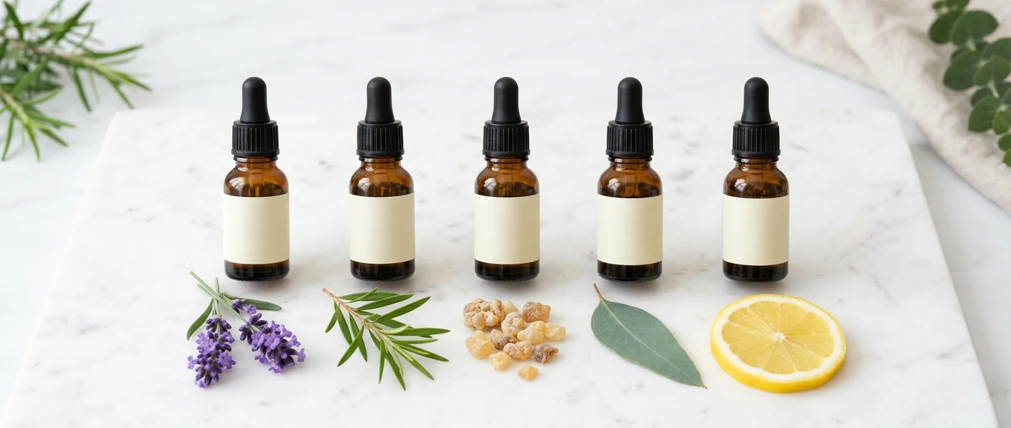 Single essential oil bottles in a row — lavender, tea tree, frankincense, eucalyptus and lemon with fresh botanicals